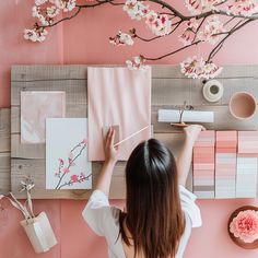 a woman is painting on the wall with pink and white flowers in front of her