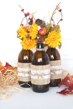 three brown vases with yellow flowers and burlap ribbon on them sitting next to straw