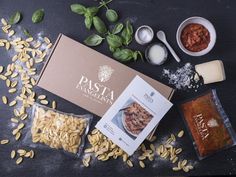 pasta ingredients laid out on top of a black surface with basil, sunflower seeds and seasonings