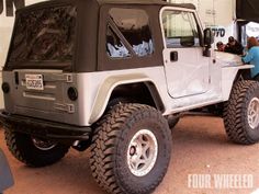 a white jeep parked in front of a building with people looking at the cars on display