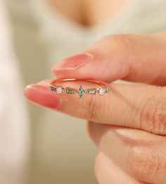 a woman's hand holding a gold ring with green and white stones on it