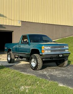 a blue pick up truck parked in front of a building with two large tires on it