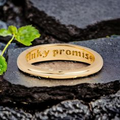 a gold ring that says, pinky proma on it next to a plant