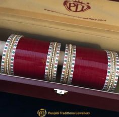 two red bangles are in a box with gold trimmings on the sides