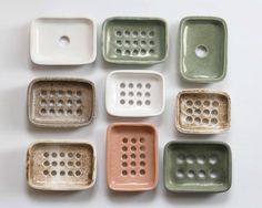 nine ceramic trays with holes in them on a white surface, one is green and the other is pink