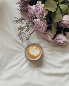 there is a cup of coffee and some flowers on the white sheet next to it