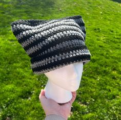 a person holding up a knitted hat on top of a mannequin head