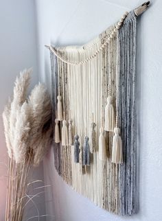 a wall hanging made out of macrame beads and tassels, with a plant in the foreground