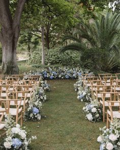 an outdoor ceremony setup with blue and white flowers, greenery, and wooden chairs