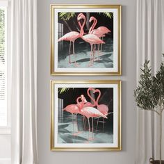 two pink flamingos standing next to each other in front of a white wall with gold frames