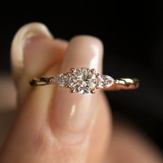 a woman's hand holding an engagement ring with three stones on the top and bottom