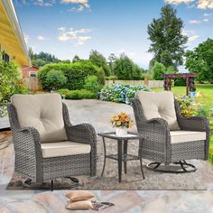 two wicker chairs and a table on a stone patio with flowers in the background