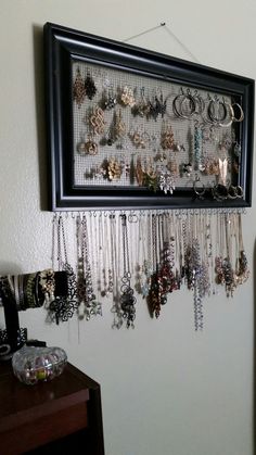 there is a black frame hanging on the wall with many different necklaces attached to it