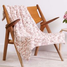 a chair with a blanket on it next to a flower vase and wooden chairs in front of a white wall