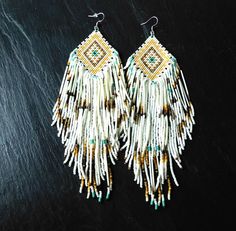 two pairs of beaded earrings on top of a black surface with gold and white beads