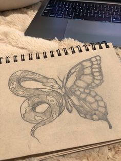 a drawing of a butterfly and a snake on top of a notebook next to a laptop