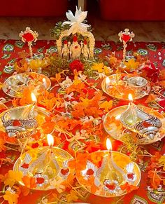 a table topped with lots of silver plates covered in flowers and lit candles on top of it