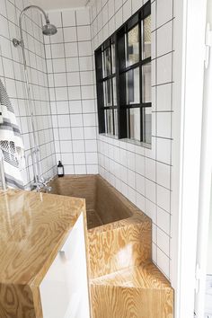 a bathroom with white tiled walls and wooden steps leading up to the bathtub area