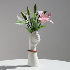 a white vase with flowers in it and a hand holding the flower up to its side