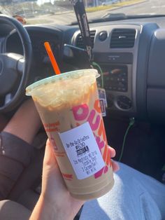 a person is holding up a drink in their hand and steering wheel behind the car