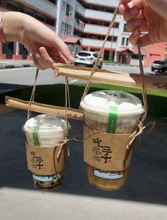 two people holding up coffee cups in brown paper bags with string attached to the handles