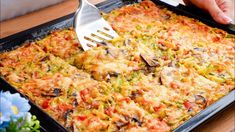 a person holding a spatula over a casserole dish with vegetables and cheese