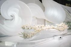 an artistic display with white flowers in vases and large sculptures on the wall behind it