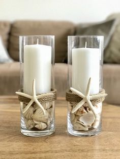 two candles with seashells and starfish in them on a table next to a couch