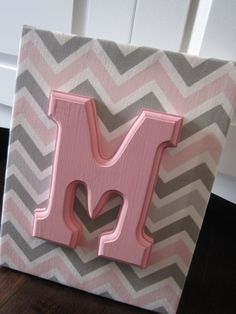 the letter m is painted pink and grey chevrons on a wood block with a wooden