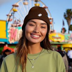 a young woman wearing a beanie smiles at the camera in front of an amusement park