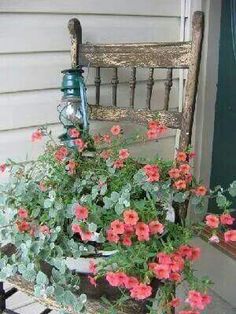 a wooden chair sitting on top of a porch next to a flower pot filled with red flowers