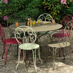 an outdoor table and chairs are set up on the stone ground in front of some bushes