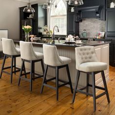 a kitchen with black cabinets and white counter tops, four stools at the island