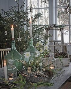 a table topped with green vases filled with flowers and candles next to a christmas tree