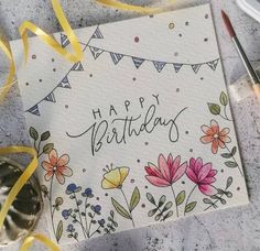 a happy birthday card with flowers and buntings on it next to some paintbrushes