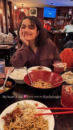 a woman sitting at a table with plates of food and chopsticks in front of her