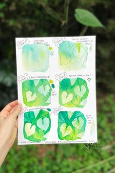 a hand holding up a piece of paper with watercolor on it and green leaves