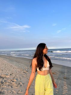 a woman walking on the beach with her surfboard in hand and looking up at the sky