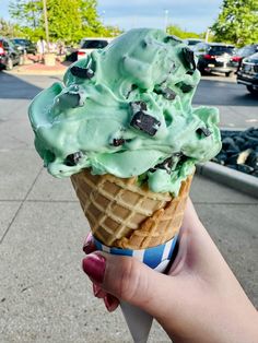 a hand holding an ice cream cone filled with mint green chocolate chip cookies and oreo chunks