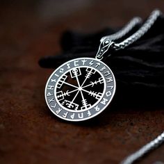 a silver compass necklace sitting on top of a black cloth