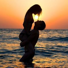 a man and woman kissing in the ocean at sunset, with the sun setting behind them