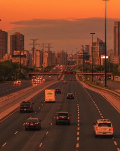 cars are driving down the highway with tall buildings in the backgrouds at sunset