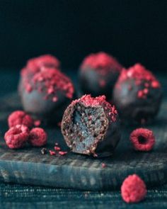 chocolate truffles with red sprinkles are on a table next to raspberries