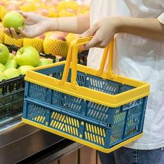 a woman holding a yellow and blue shopping basket in front of some fruit on display