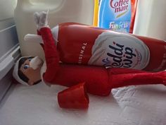 an elf laying on top of a refrigerator next to a bottle of soft drink and a toothbrush