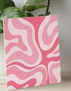 a pink and white abstract painting on a wooden table next to a potted plant