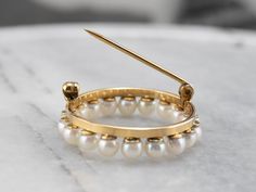 This vintage pearl circle brooch is a true classic! Simple and refined, traditional white pearls form a shimmering wreath, backed by rich yellow gold. This brooch would look wonderful pinned to a scarf or lapel, or even on a bridal bouquet! Love this piece but want to make it more versatile? We here at Market Square Jewelers, along with our master metalsmiths can convert this fantastic brooch into a necklace or pendant for an additional fee. Please contact us for more information! Metal: 10K Yel Timeless Wedding Brooch Jewelry, Classic Gold Round Brooches, Classic Round Jewelry Brooch, Elegant Yellow Gold Round Brooches, Classic Yellow Gold Brooches For Wedding, Classic Yellow Gold Round Brooches, Classic Round Yellow Gold Brooches, Classic Yellow Gold Wedding Brooches, Round Brooches With 17 Jewels For Wedding