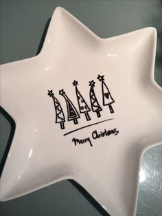 a white star shaped dish with three christmas trees on the front and merry christmas written in black