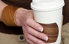 a woman's hand holding a white coffee cup with wooden sleeve wraps around her arm