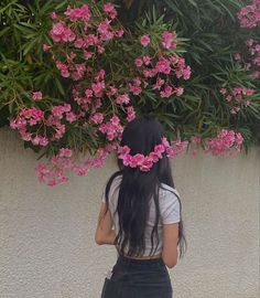 a woman with long black hair standing in front of pink flowers on a white wall